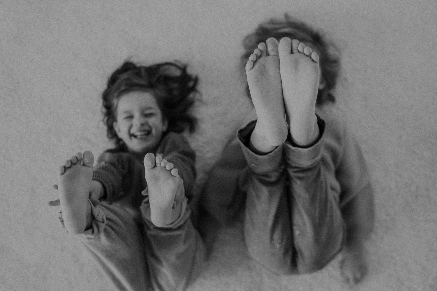 Two people lying down show their bare feet while laughing in a playful black and white photo.