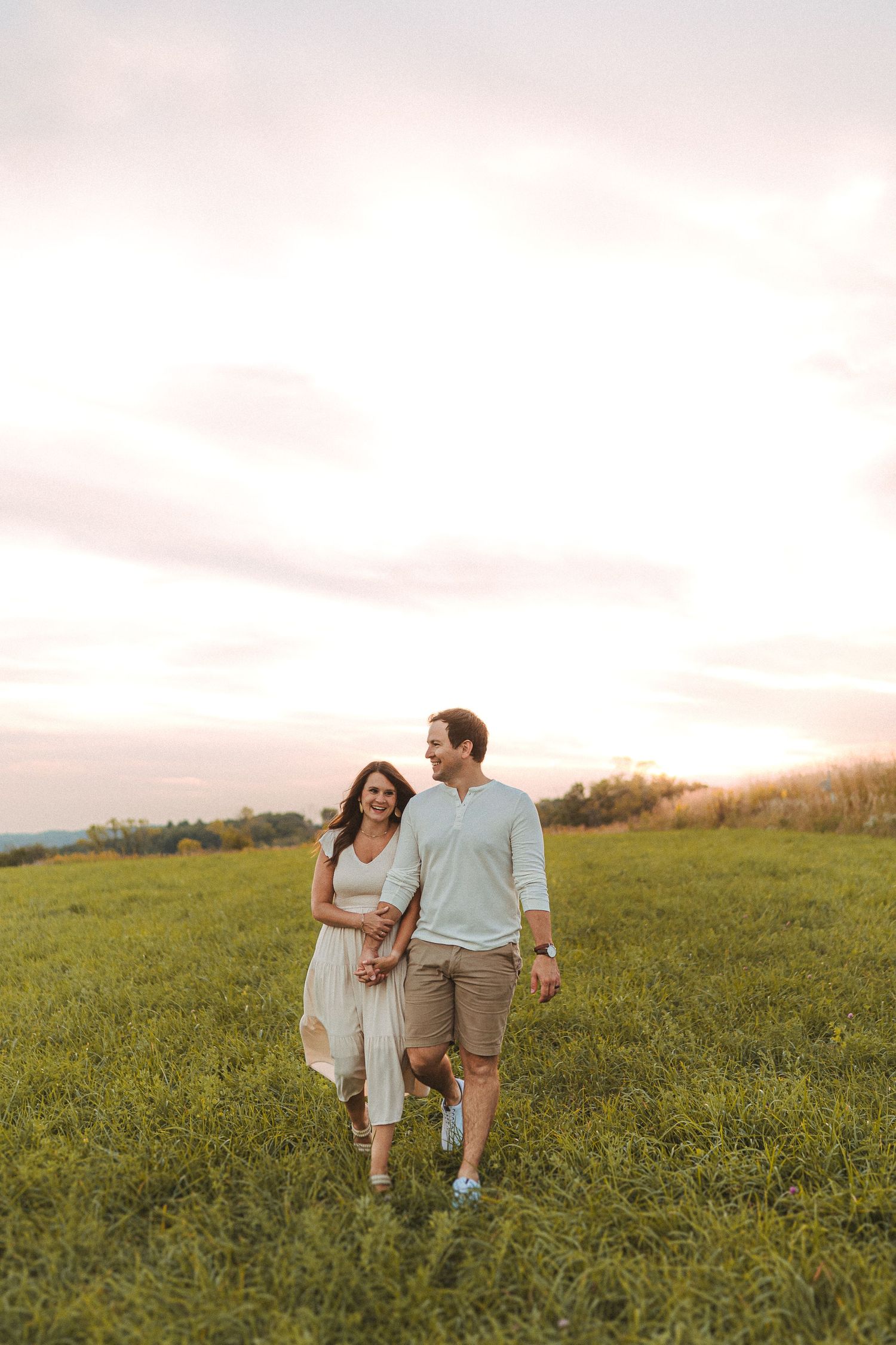 Two people stroll together through a scenic hillside field at sunset.