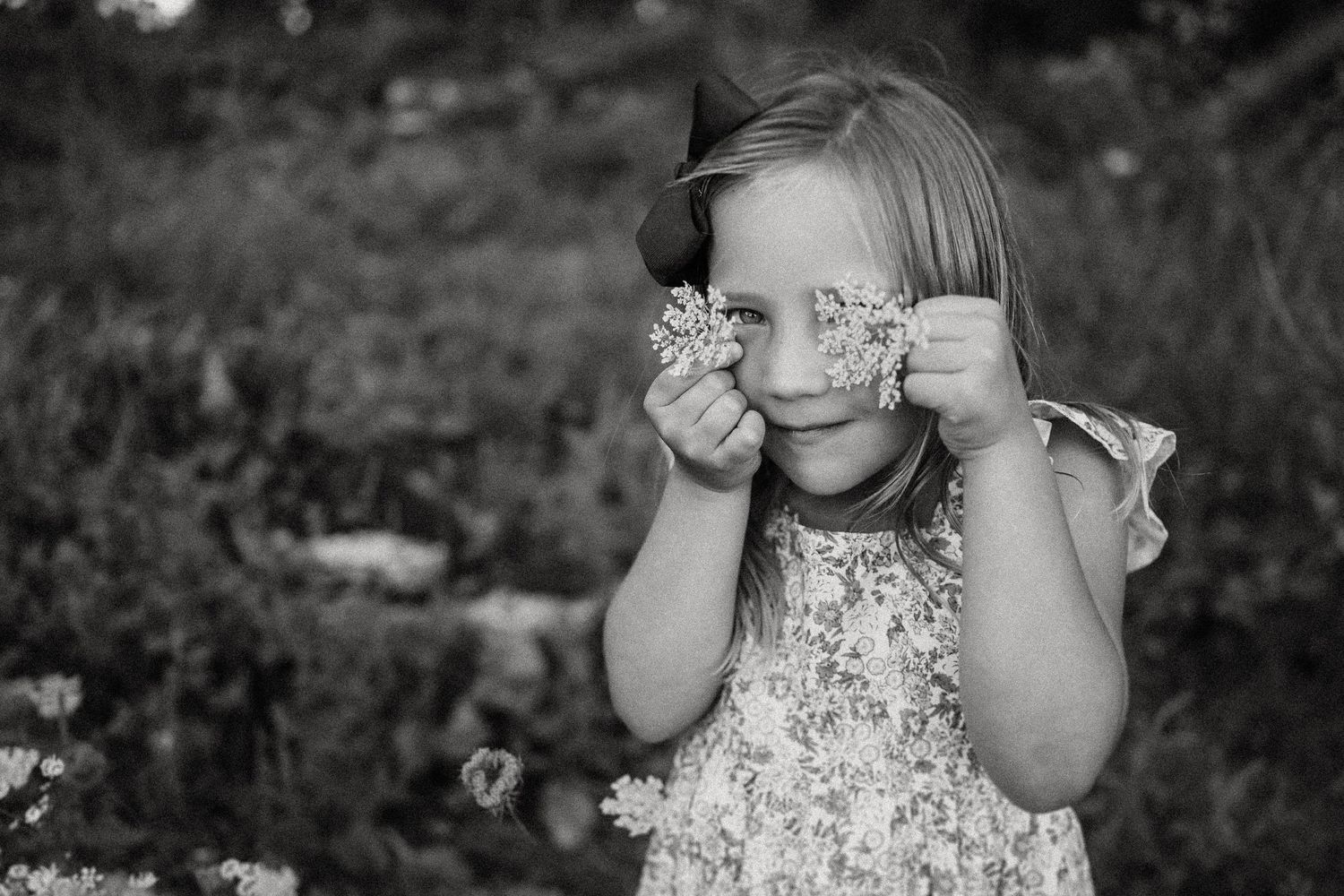 Black and white portrait of playful pose with wildflowers held up to eyes.