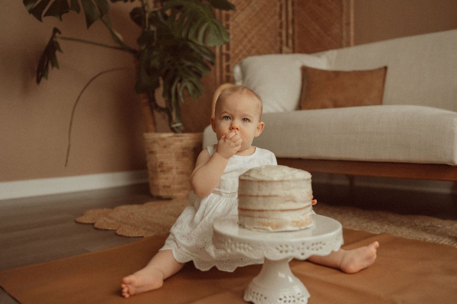A small cake smash photo session featuring a white tiered cake on a decorative stand in a cozy living room setting.