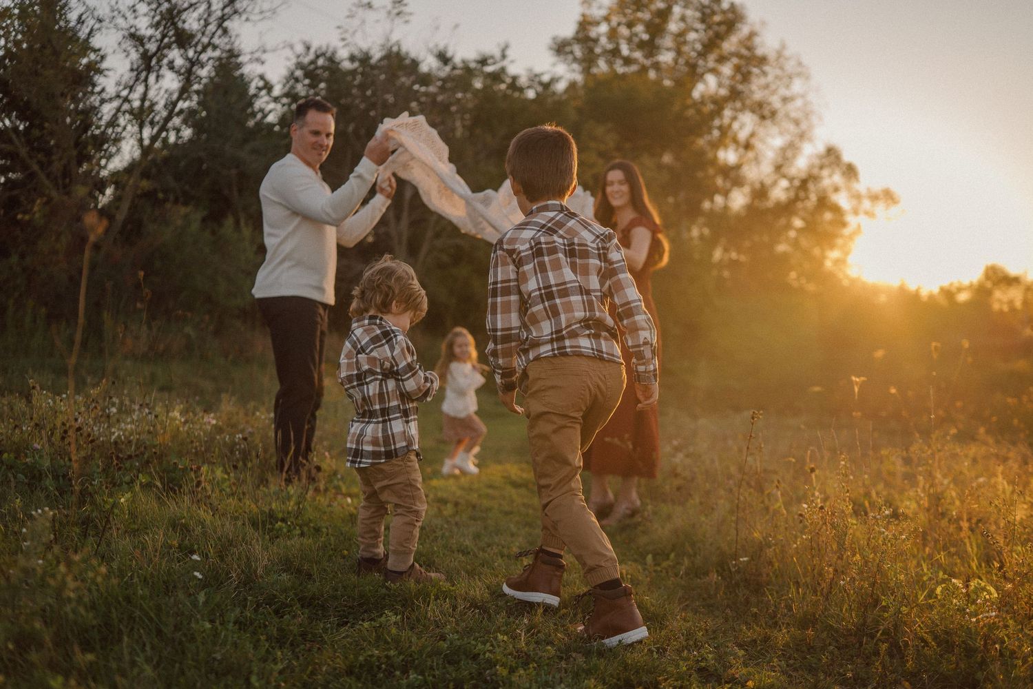 Family playing together in a golden sunset field with tall grass and wildflowers.