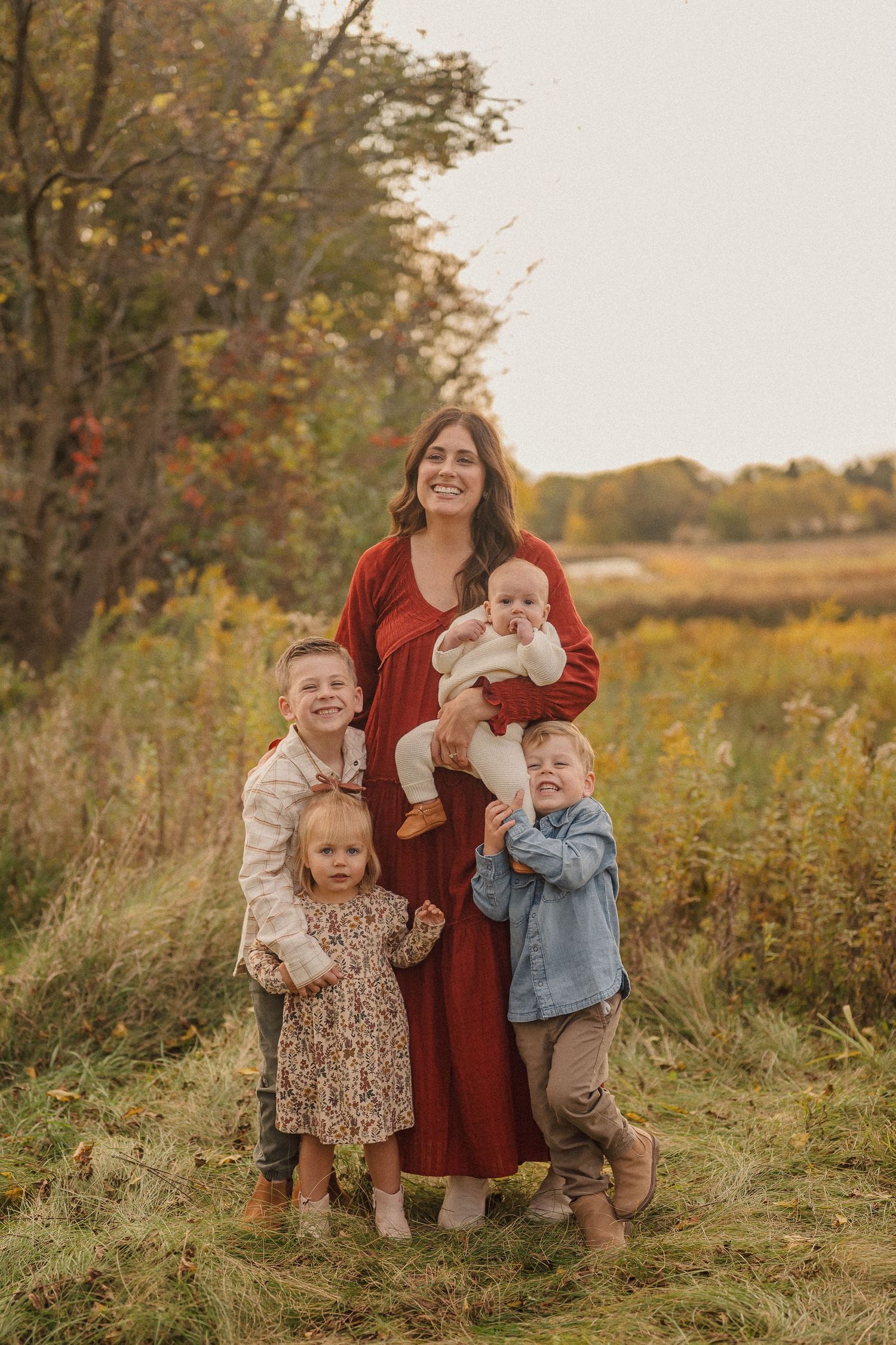 Family portrait in a golden autumn field with small children wearing rustic fall outfits.