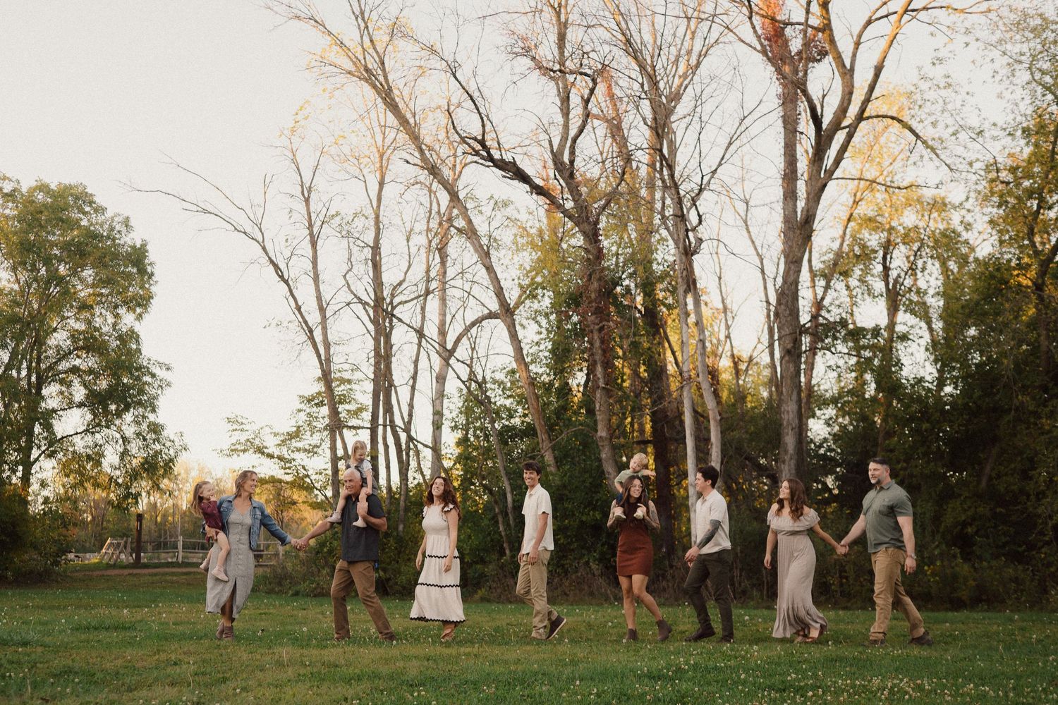 A group walks in a line through a natural outdoor setting at sunset with trees in the background.