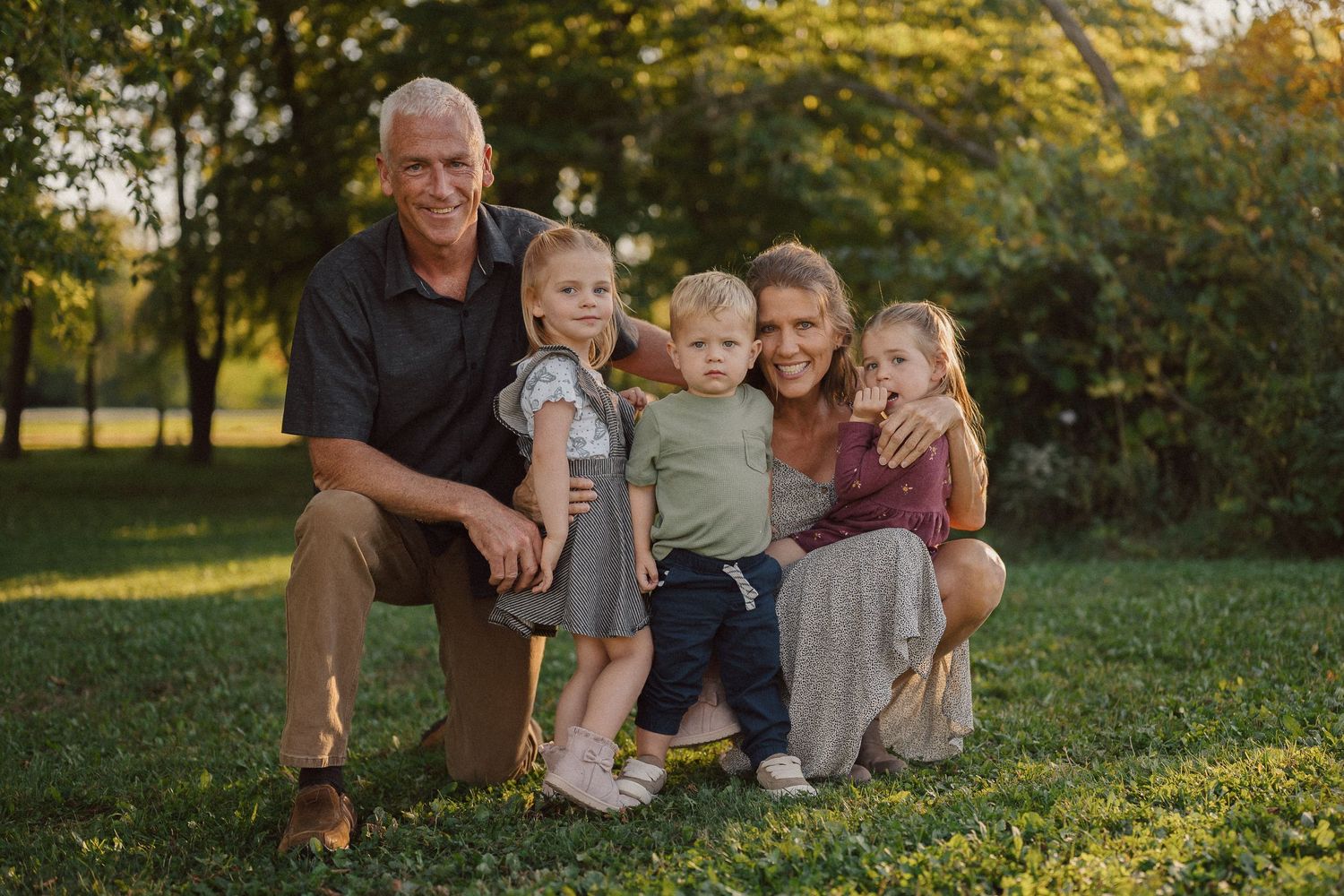 Family members sitting together on a grassy hill during sunset with fall foliage.
