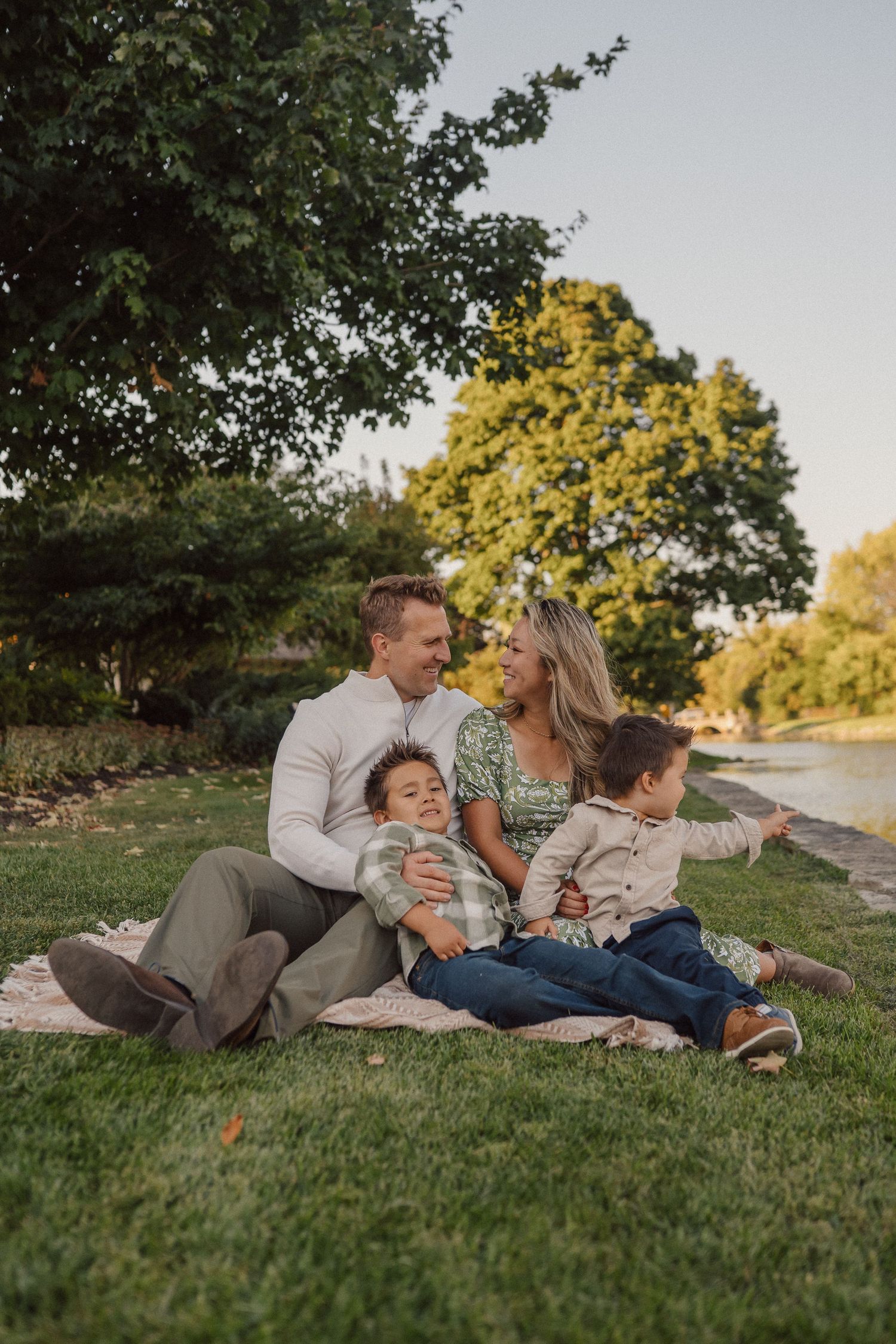 A family lounges together on green grass during a warm sunset photoshoot in a park.