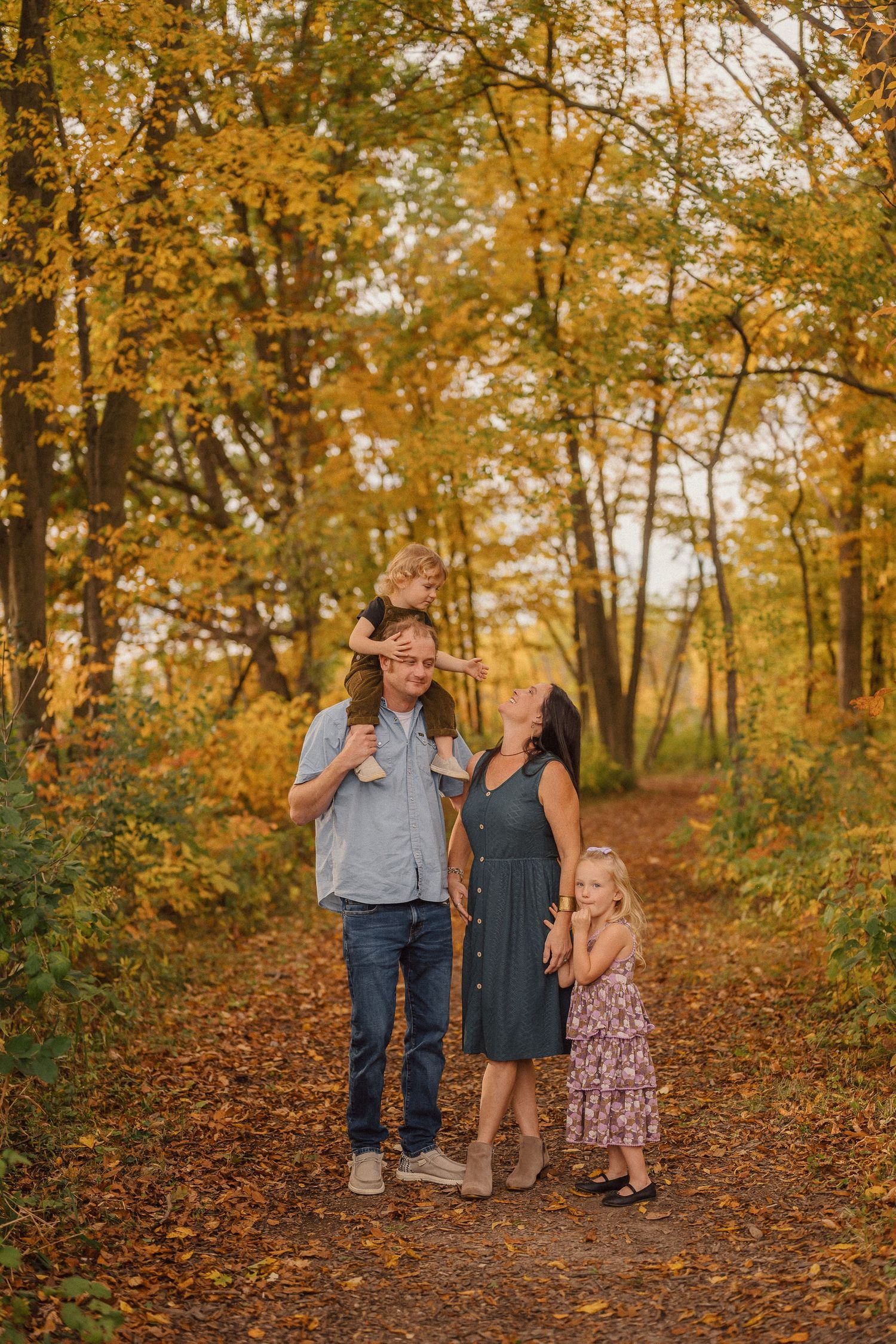 A family enjoying an autumn walk together on a leaf-covered trail surrounded by golden trees.