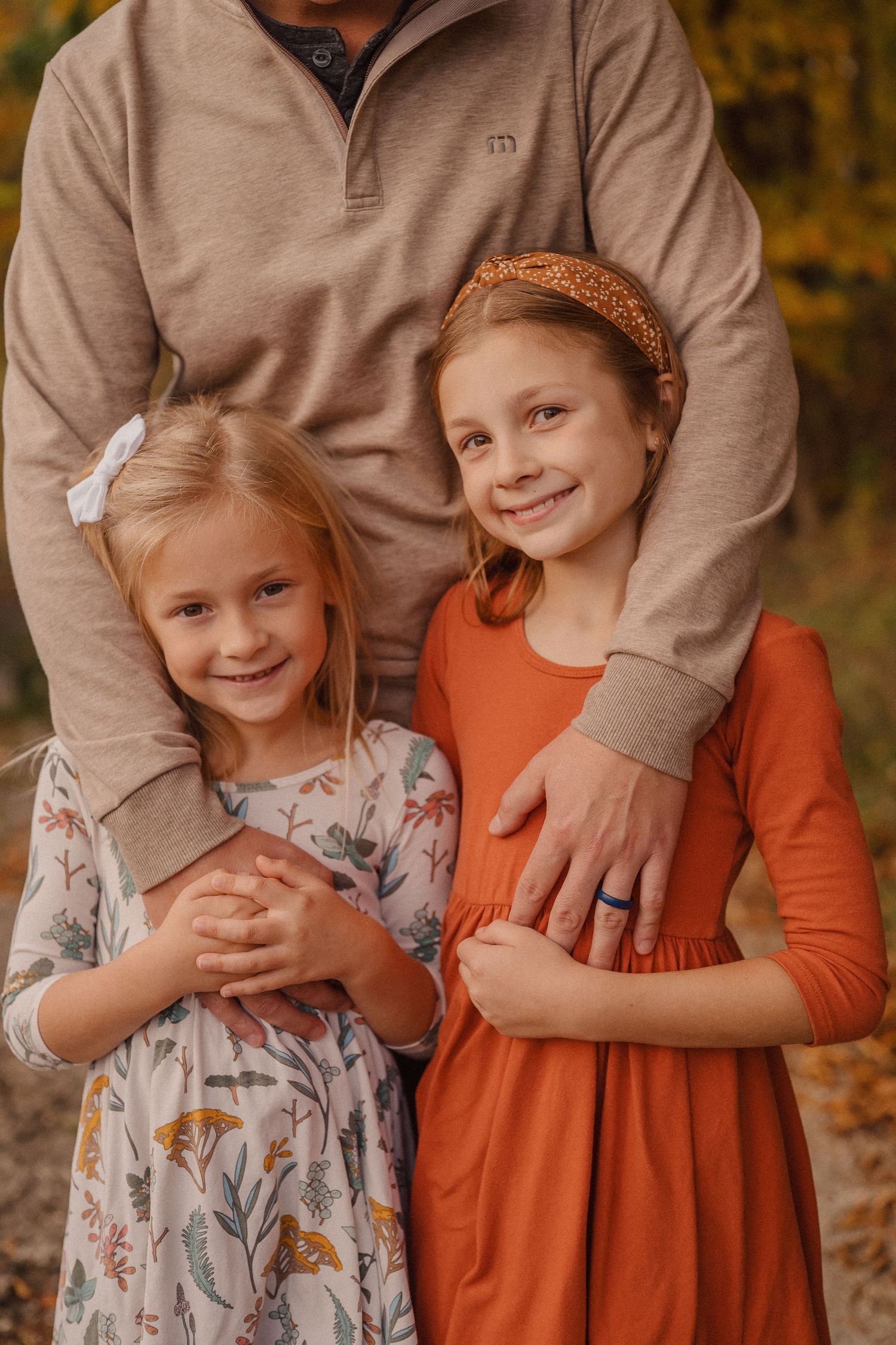 Close-up portrait showing warm embrace with tan sweater and floral dress details.