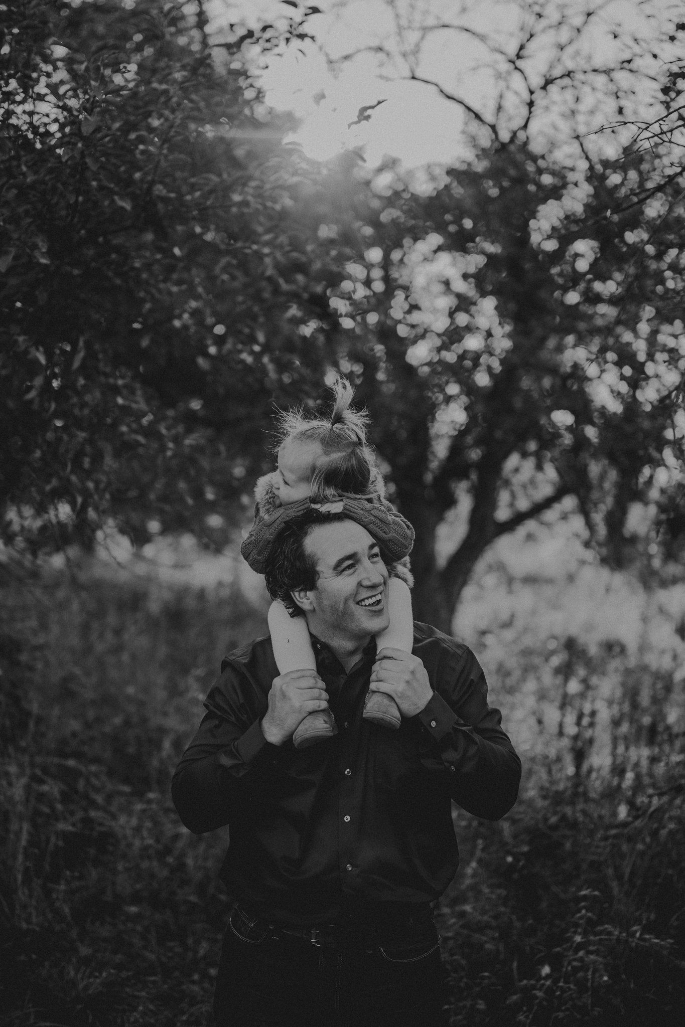 A joyful outdoor family moment captured in black and white with playful piggyback riding in a natural setting.