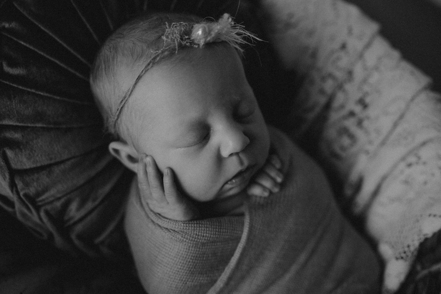 Black and white portrait of sleeping infant with delicate headpiece wrapped in soft fabric.