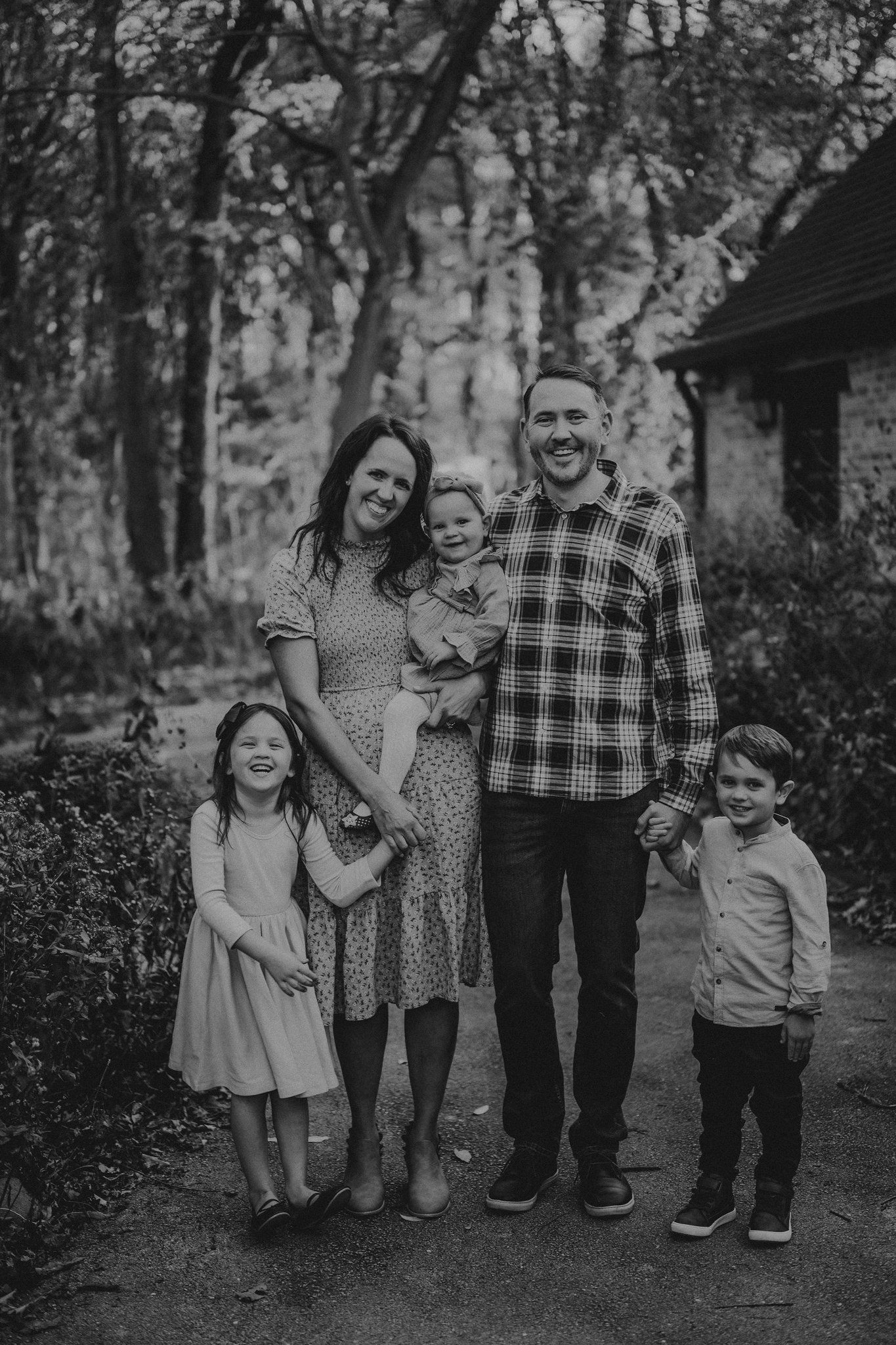 A family stands together on a wooded path in black and white photography.