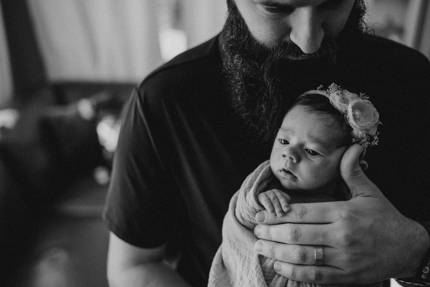 Black and white photo of an infant wearing a headband being cradled in gentle hands.