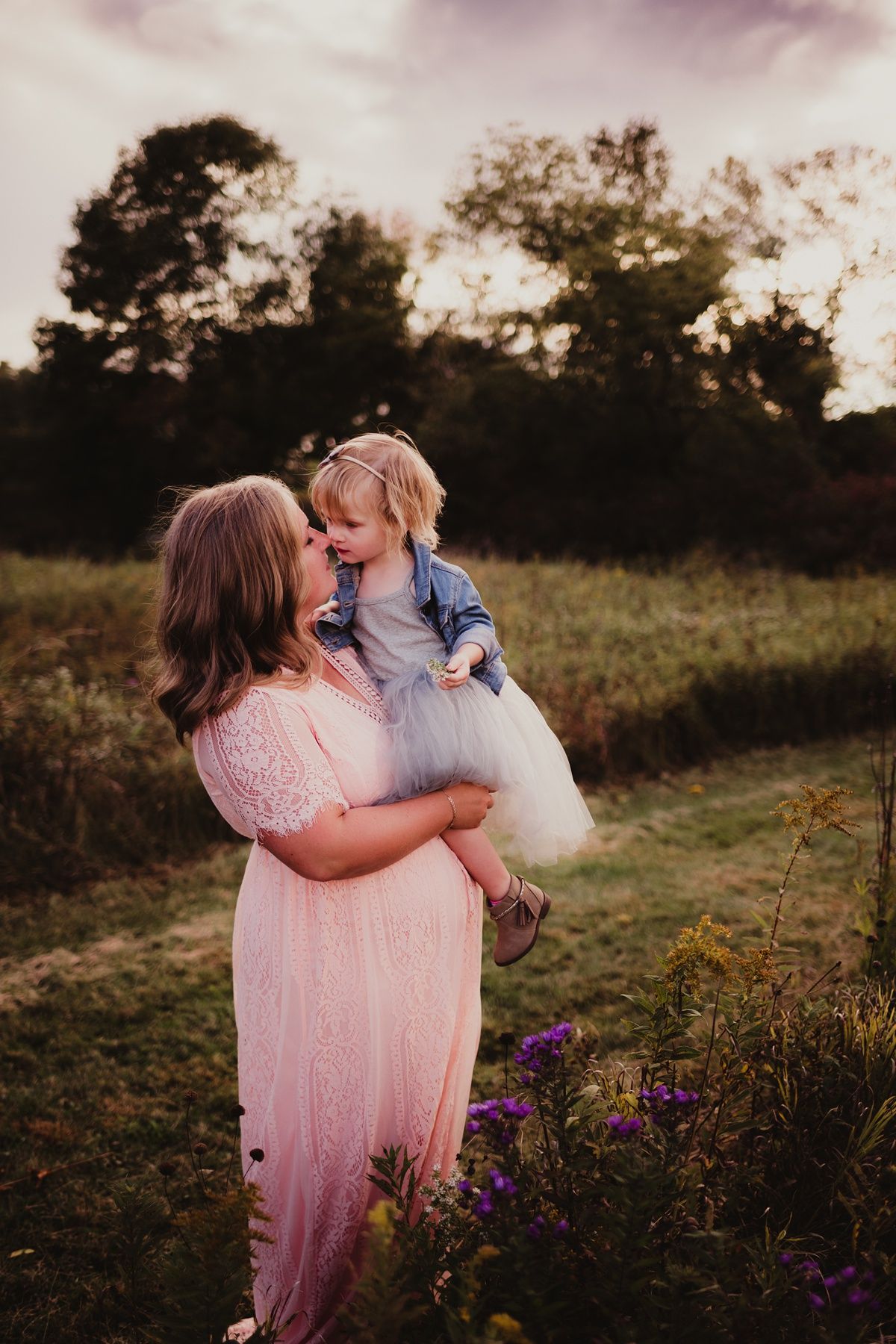 Joyful outdoor portrait of parent and child laughing together among purple wildflowers at sunset.