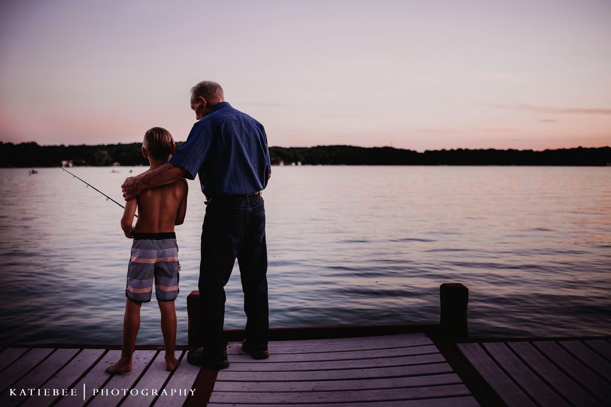 Two people standing on a dock at sunset overlooking a peaceful lake.