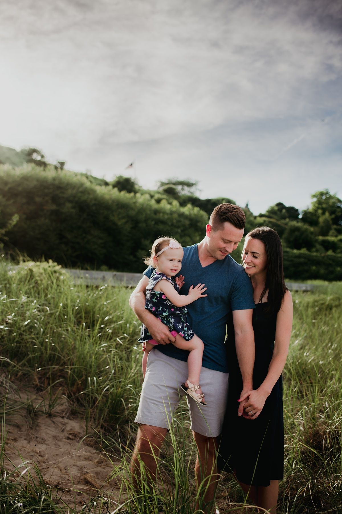 A family poses together on a grassy hillside overlooking a scenic landscape.
