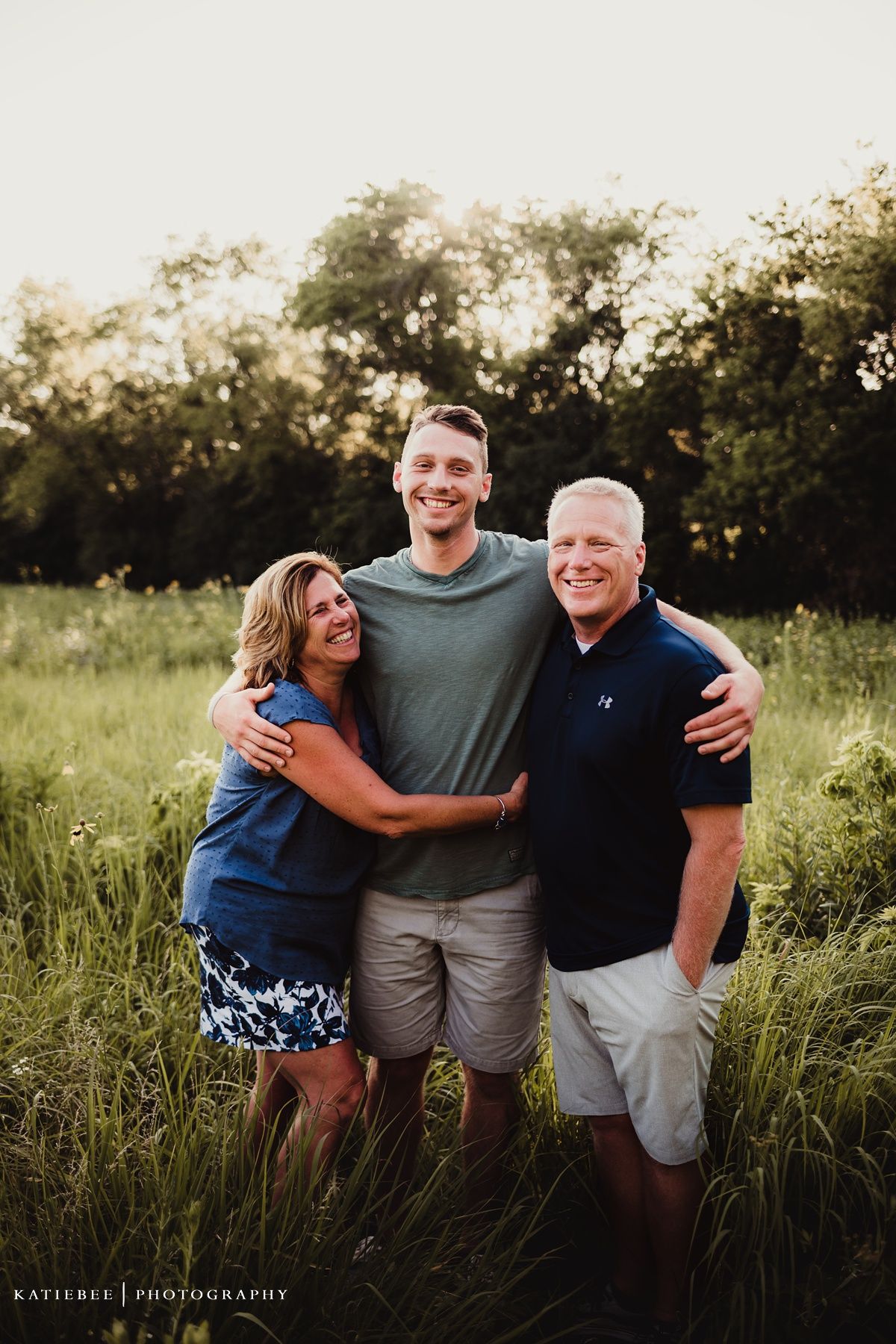 Family poses together in a sunset meadow full of tall grass and wildflowers.