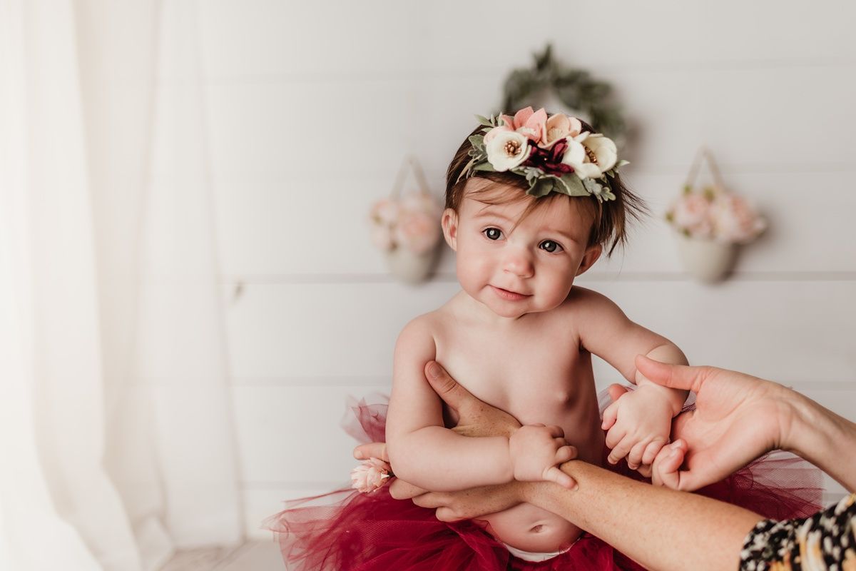 Sweet birthday portrait with floral crown and burgundy tulle tutu against white backdrop.
