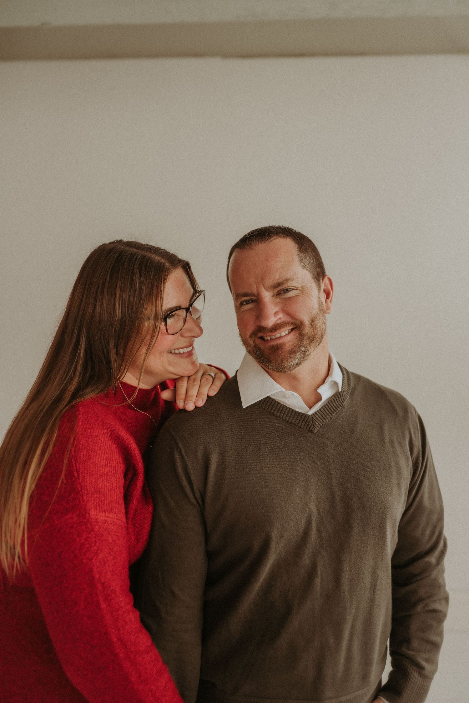 A couple shares laughter in a minimalist studio setting while wearing coordinated winter outfits.