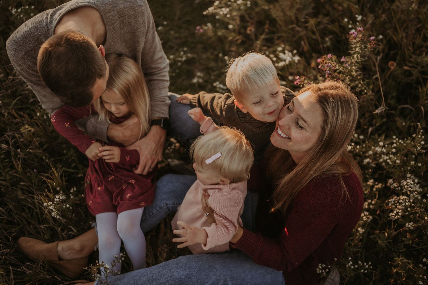 A family cuddles together outdoors in autumn wearing burgundy and neutral tones during a lifestyle photoshoot.