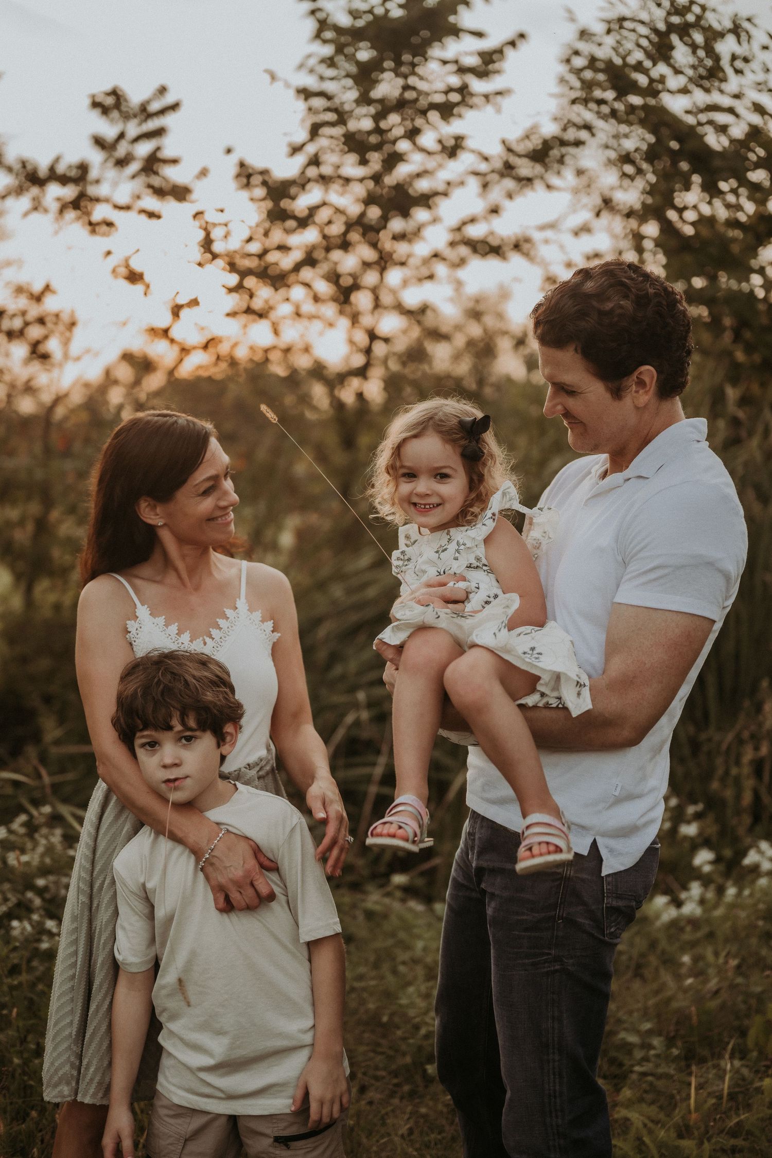 A family of four poses together in a natural outdoor setting during sunset.