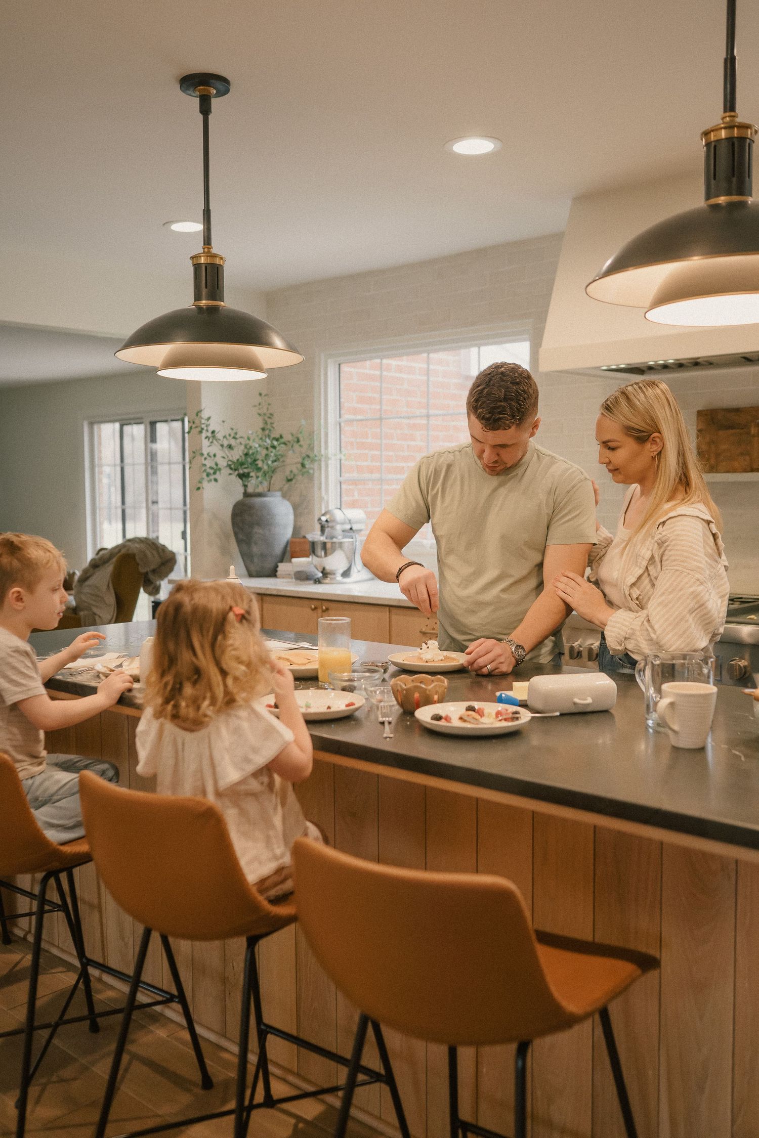 Family preparing breakfast together at a kitchen island with black pendant lights.
