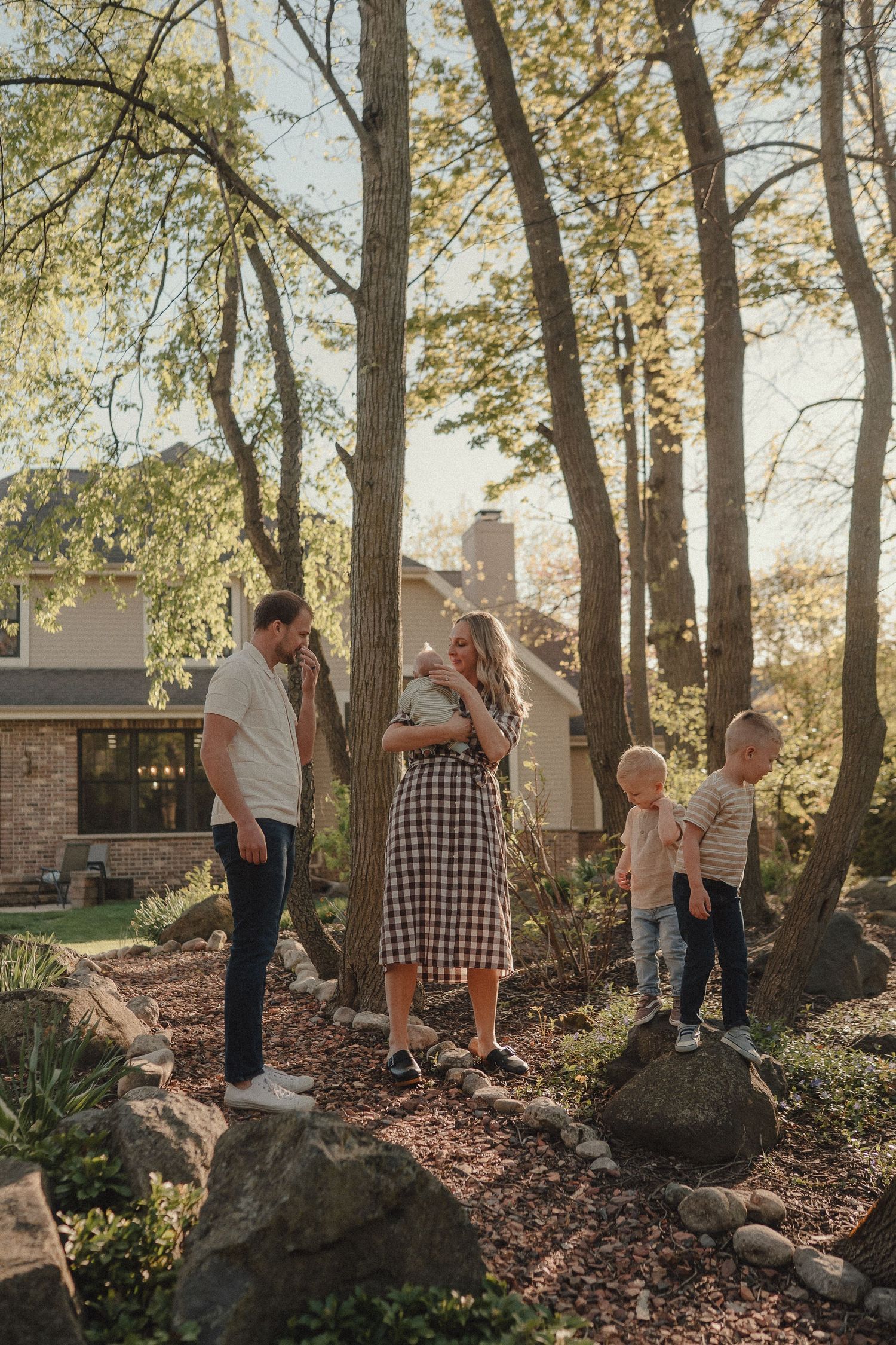 Family of four enjoying golden hour outdoors among trees and rocks near their home.