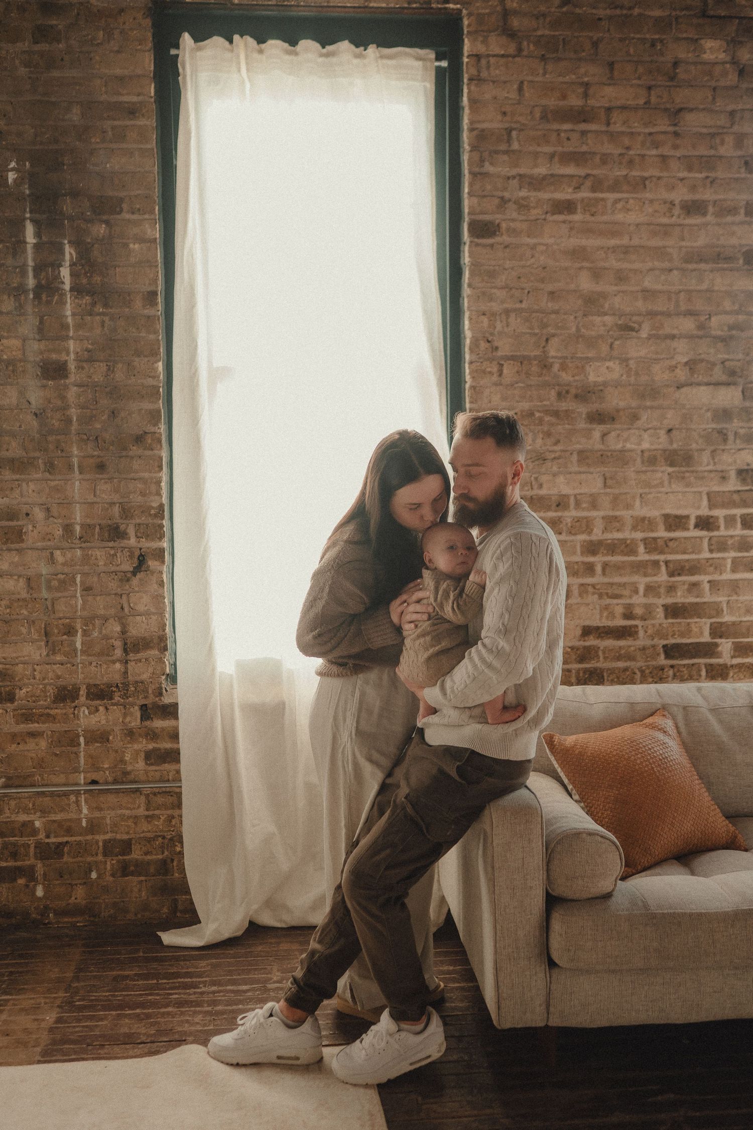Intimate moments captured on a brown leather couch against exposed brick walls in a loft setting.