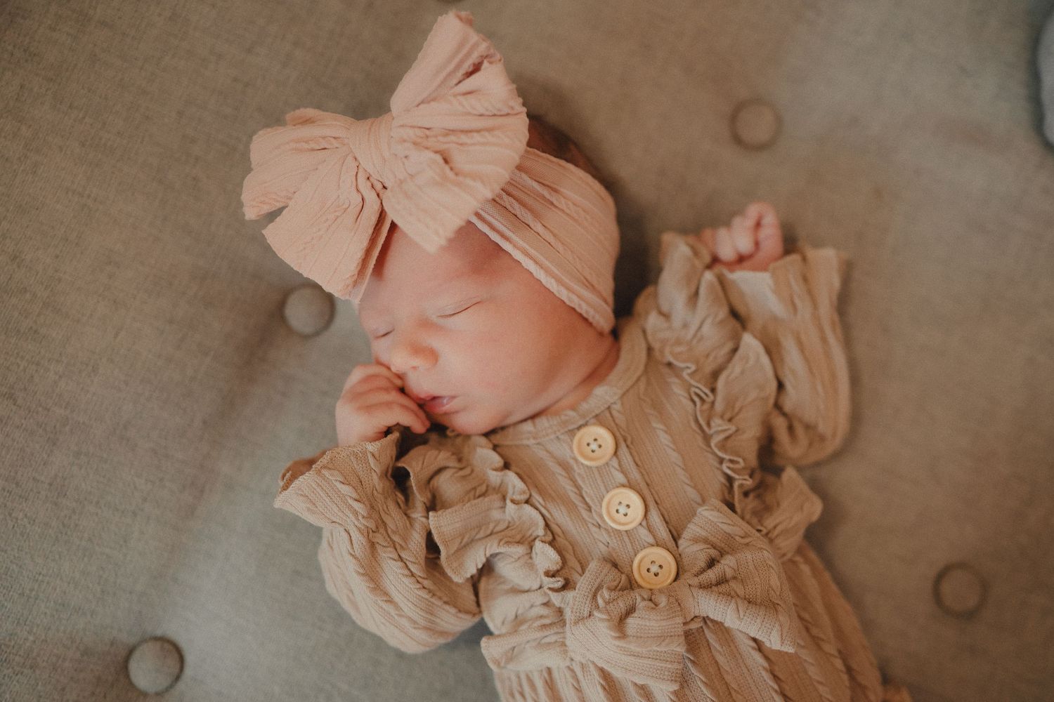 Delicate peach-colored baby clothing with ruffles and buttons laid out on neutral fabric.