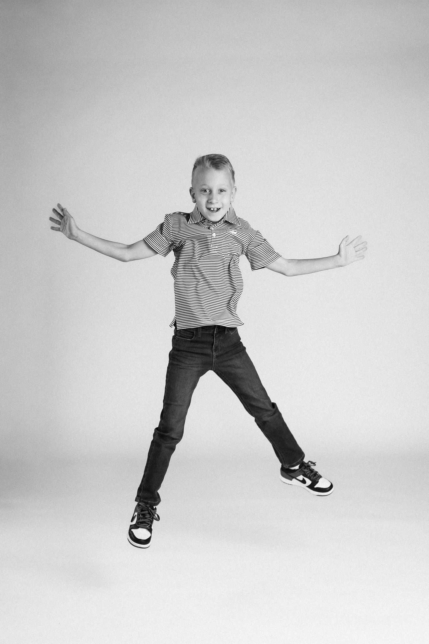 A sequence of black and white photos capturing a child in casual clothes jumping and playing with energetic movements.