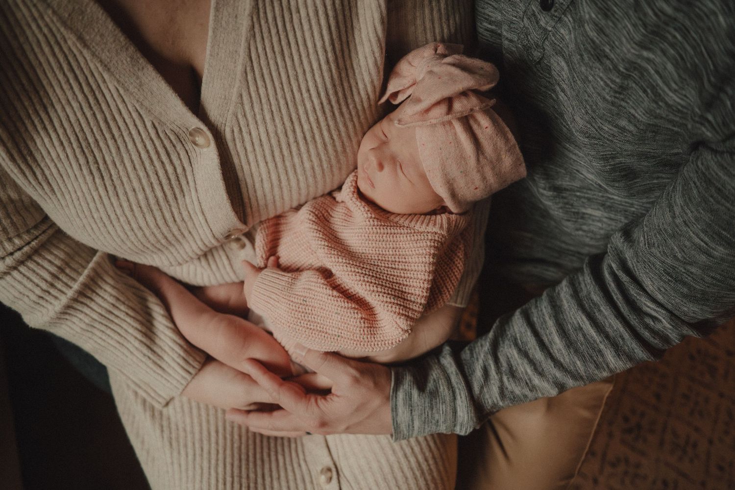 Hands gently holding and cradling a sleeping newborn baby wrapped in soft blankets.