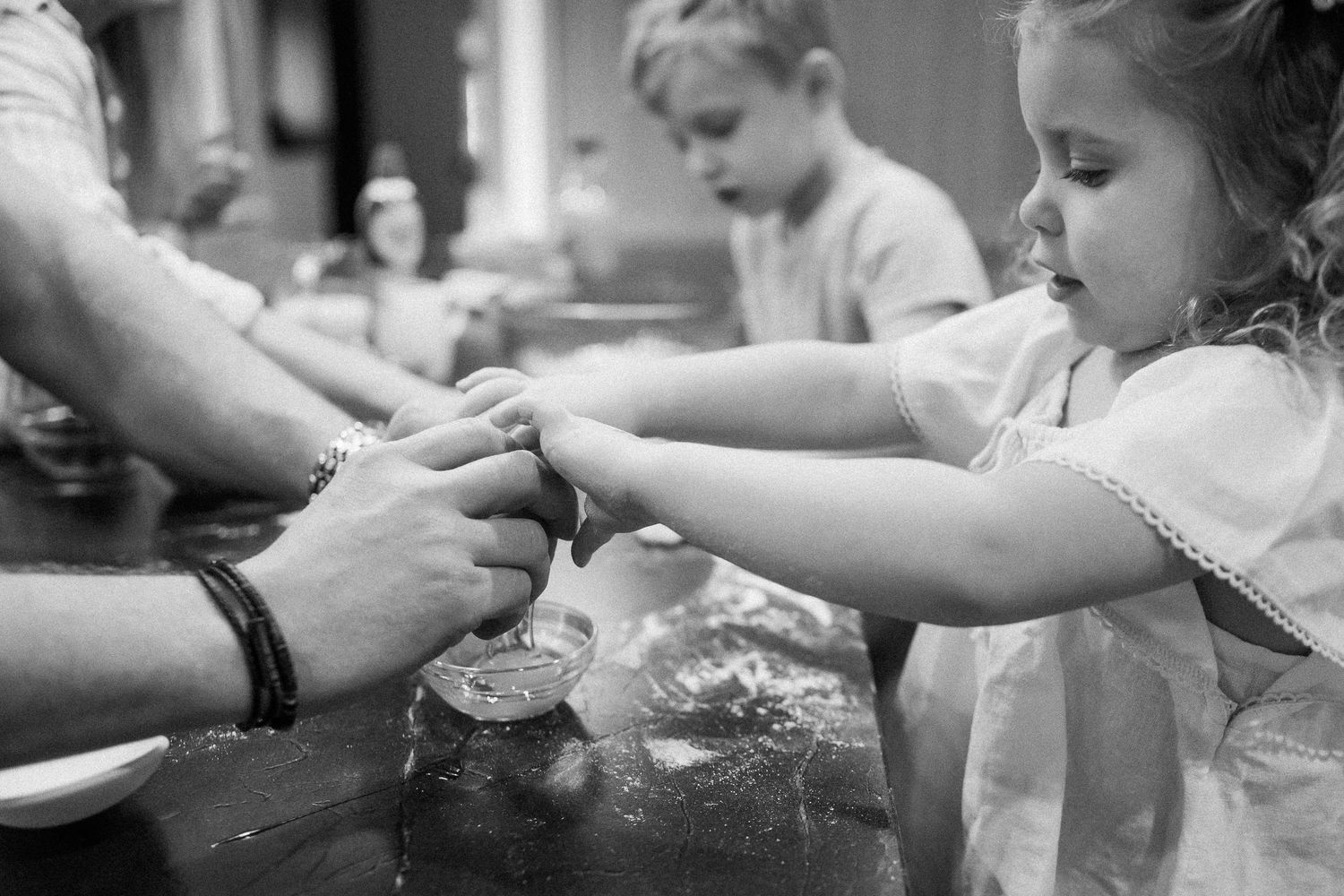 Young girl learning to bake with adult hands guiding her at kitchen counter.