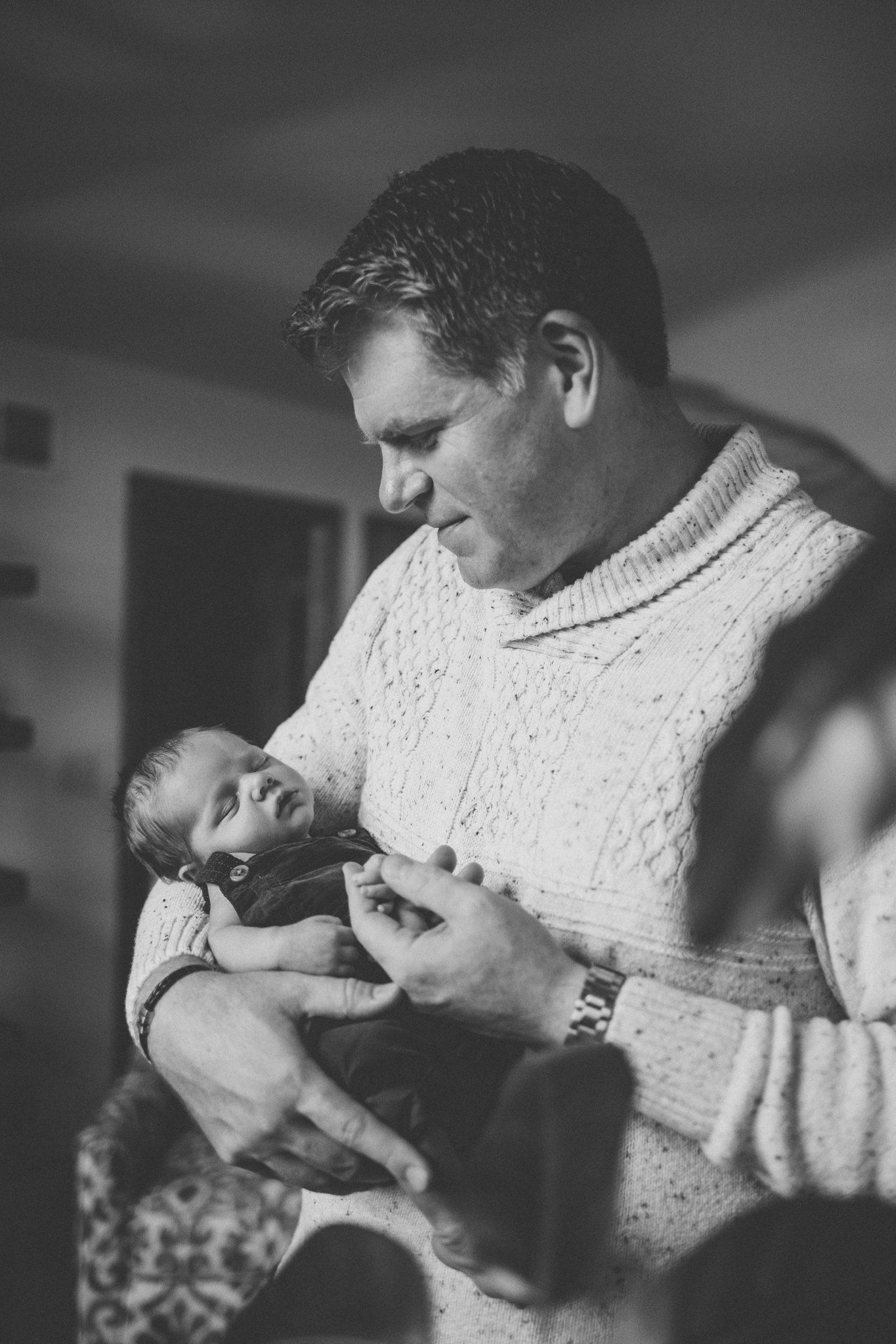 A tender black and white moment showing a parent in a cable knit sweater holding and gazing at a newborn baby.