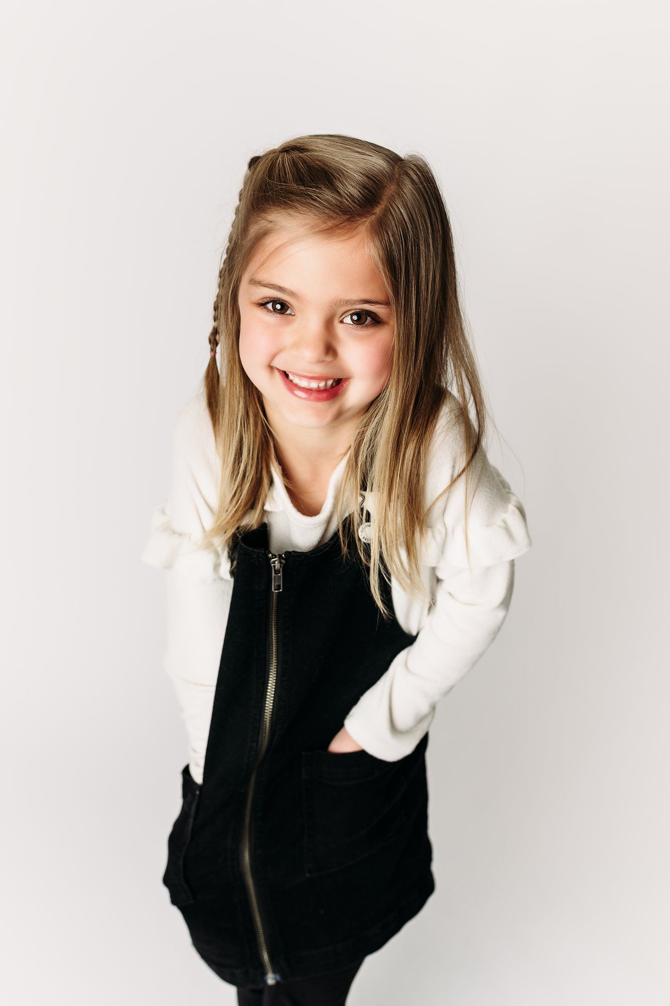 Child in black and white outfit smiling brightly against white background.