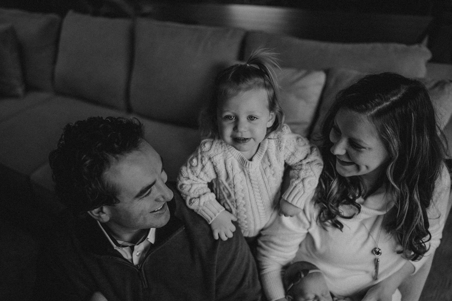 Black and white lifestyle photo of family sharing a joyful moment on couch.