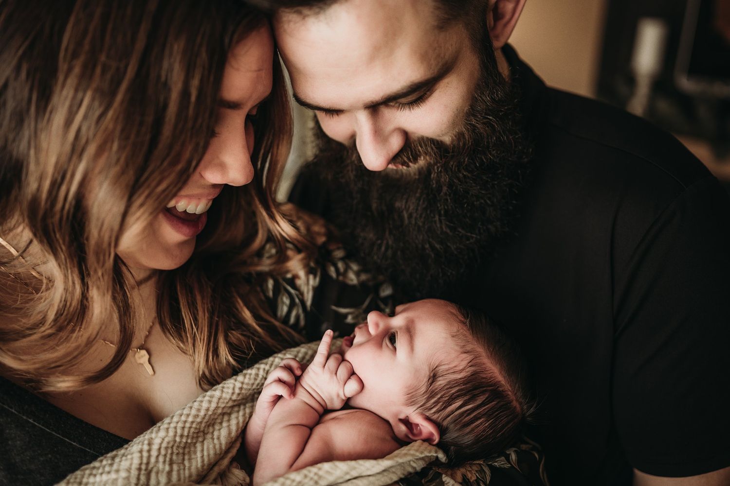 A family shares an intimate moment with their newborn baby swaddled in a knit blanket.