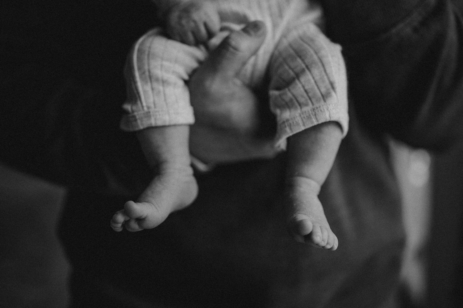 Black and white detail shot of tiny baby feet and legs in knit clothing.