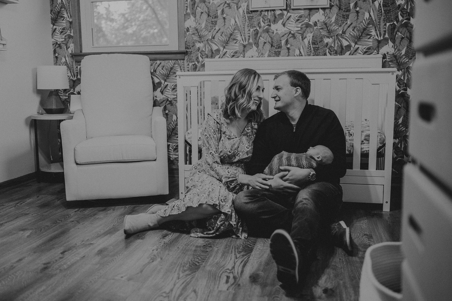 Black and white image of tender family moment in modern nursery with floral wallpaper.