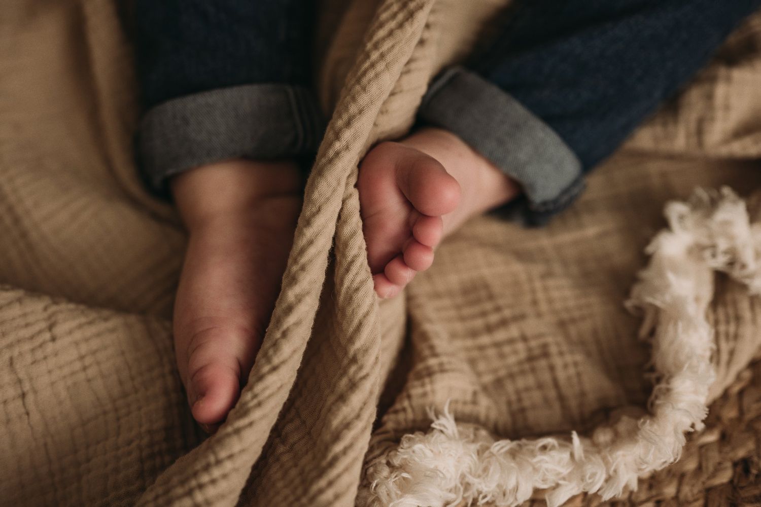 Artistic close-up of tiny feet and rope details on a neutral textile background.