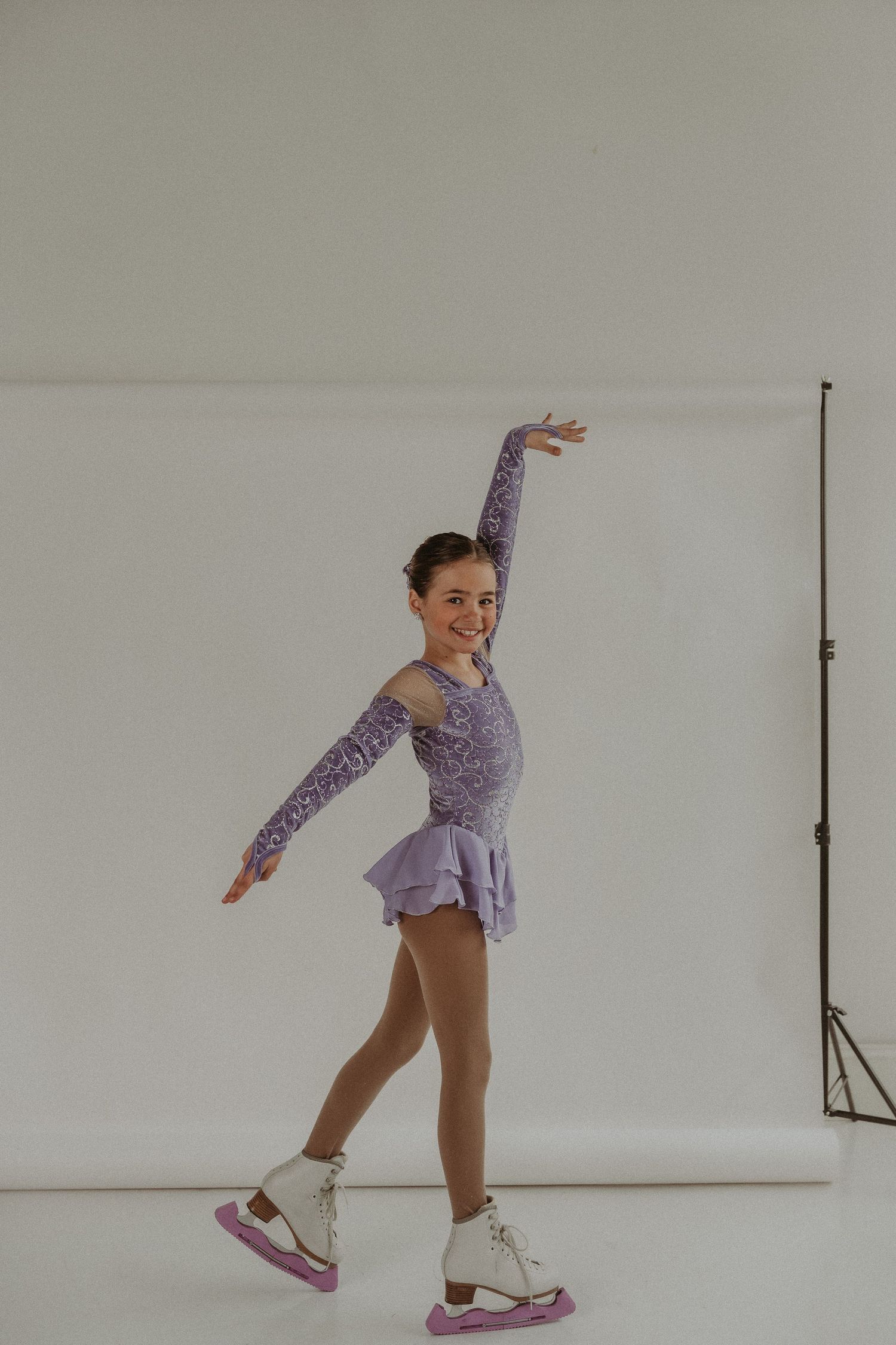 Young figure skater performing graceful skating pose in purple costume.