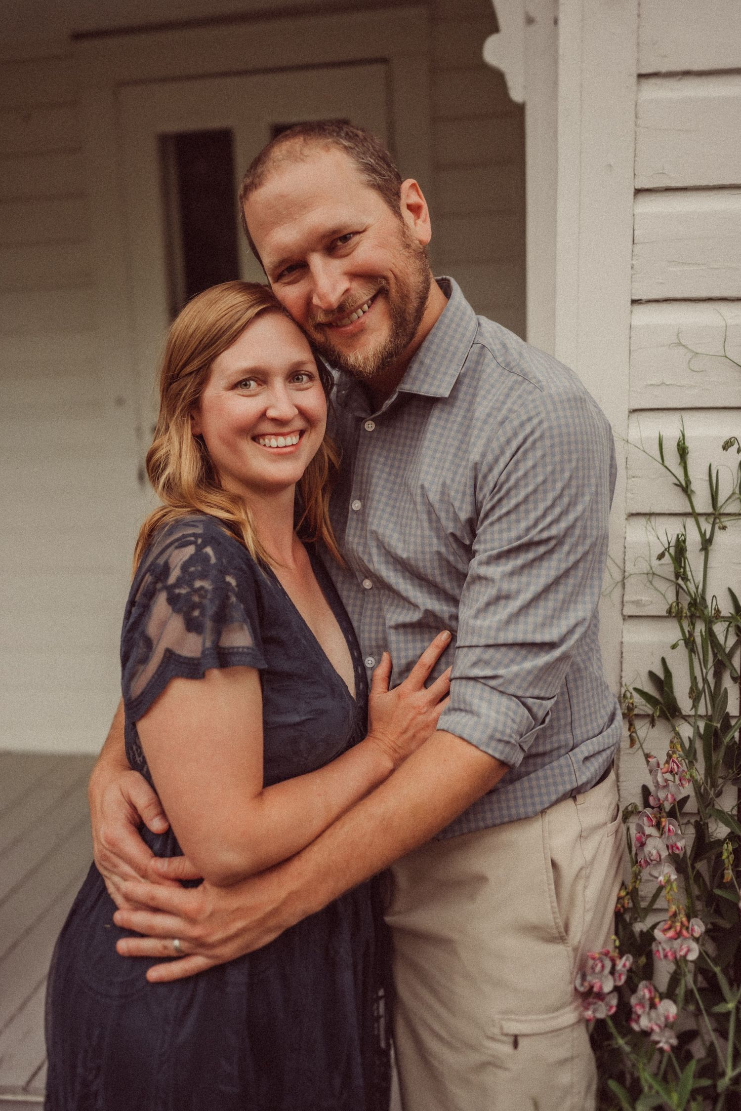 Couple embracing and smiling on porch of white farmhouse.