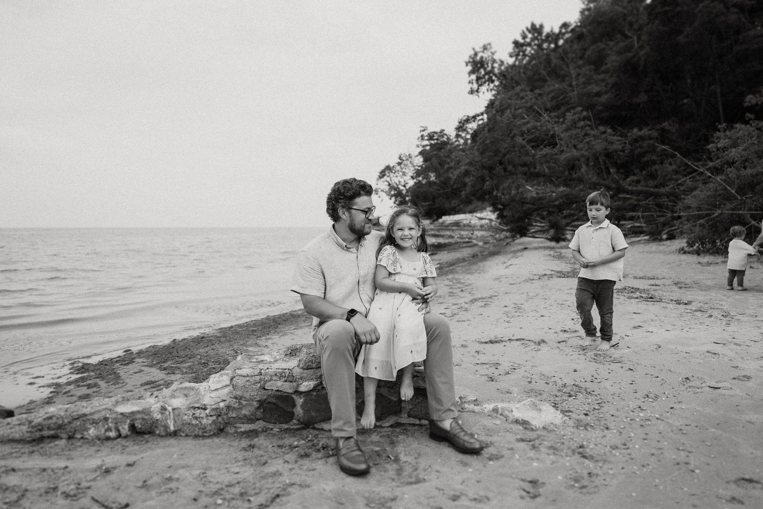 A black and white beach portrait of people sitting on rocky shore.