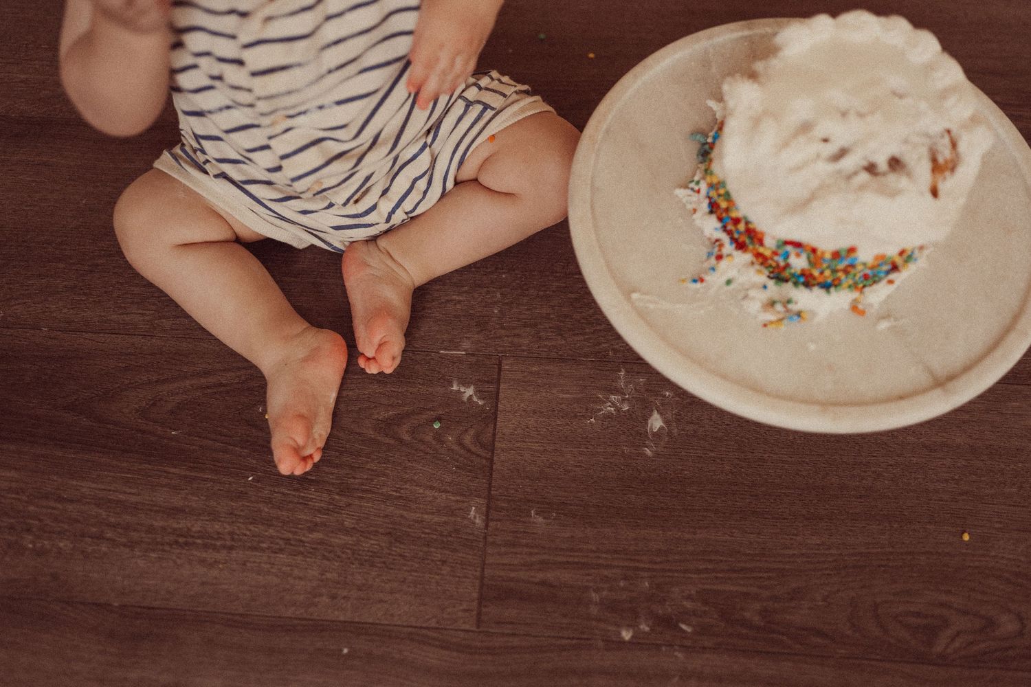 Detail shot of small feet and cake with colorful sprinkles on wooden floor.