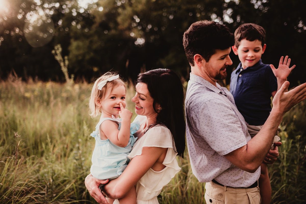 Happy family enjoying playful moments together in a sunlit field at golden hour.