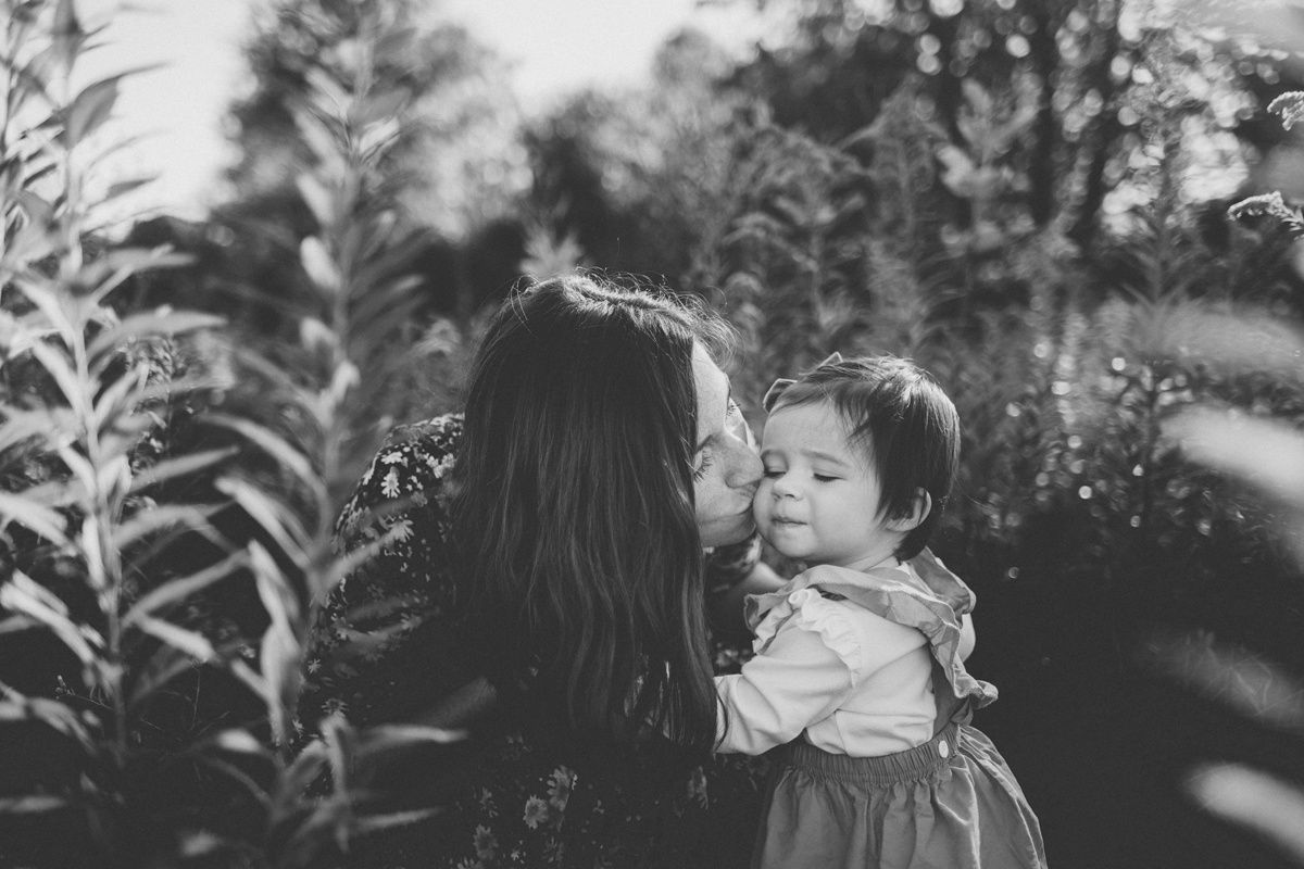A monochrome photograph showing an embrace between adult and child among tall plants.