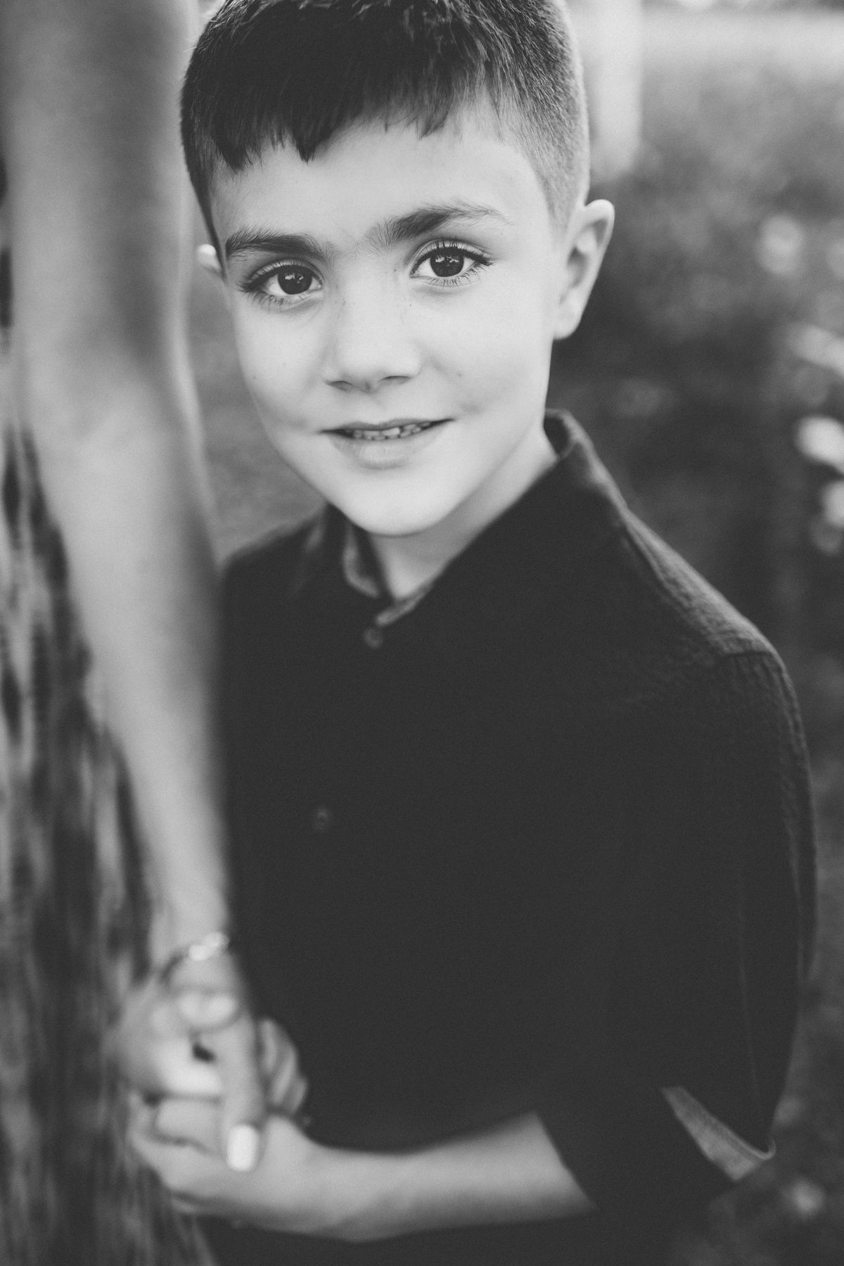 Black and white portrait of child in dark shirt against natural background.