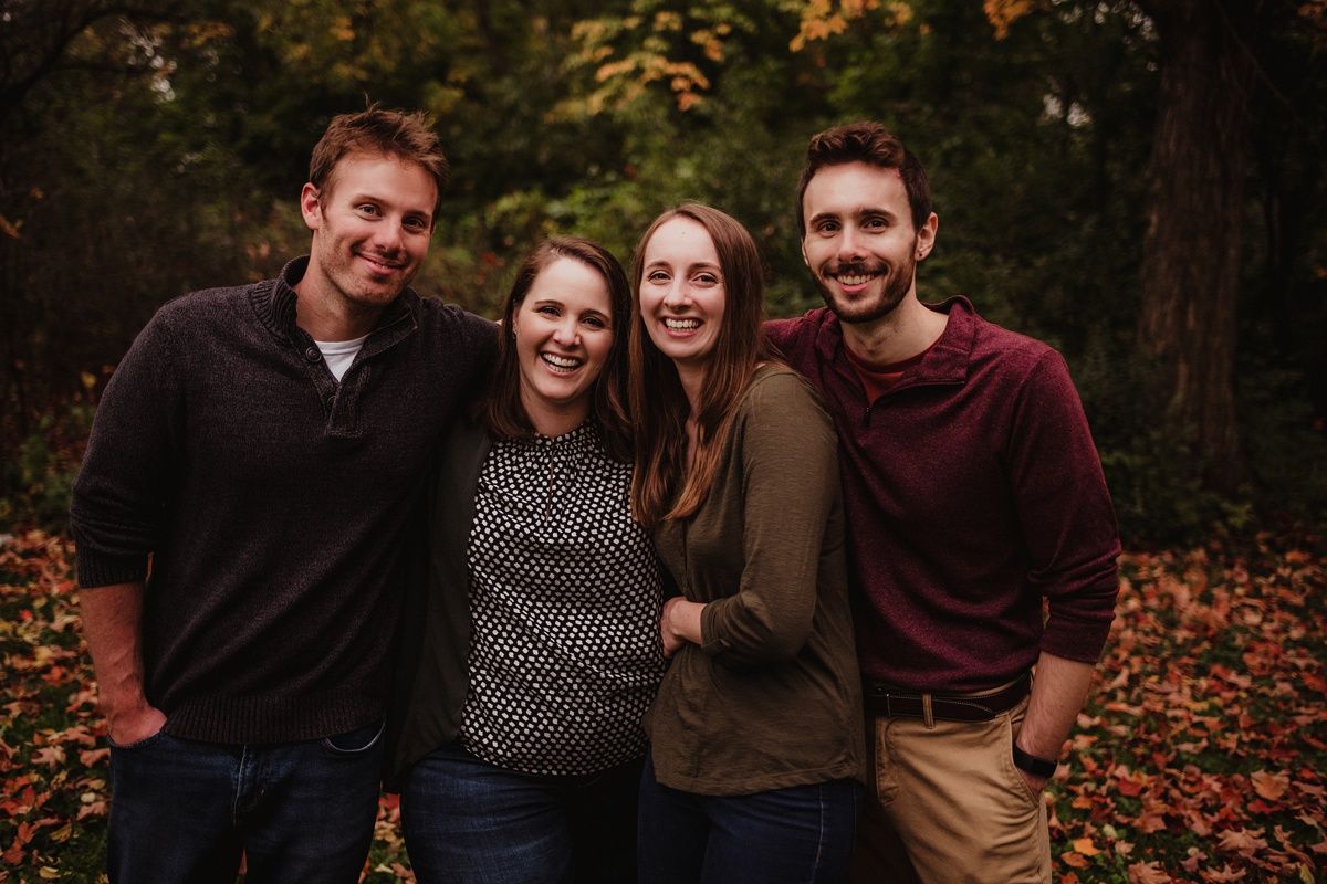 Small group portrait of four people outdoors with autumn foliage in background.