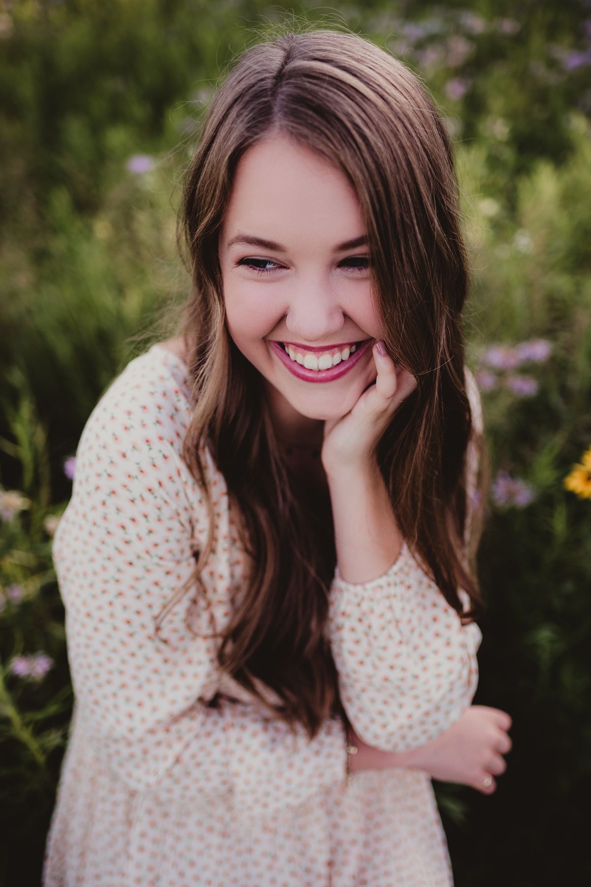 Candid outdoor portrait showing joyful laughter in a floral garden setting wearing a cream dress.