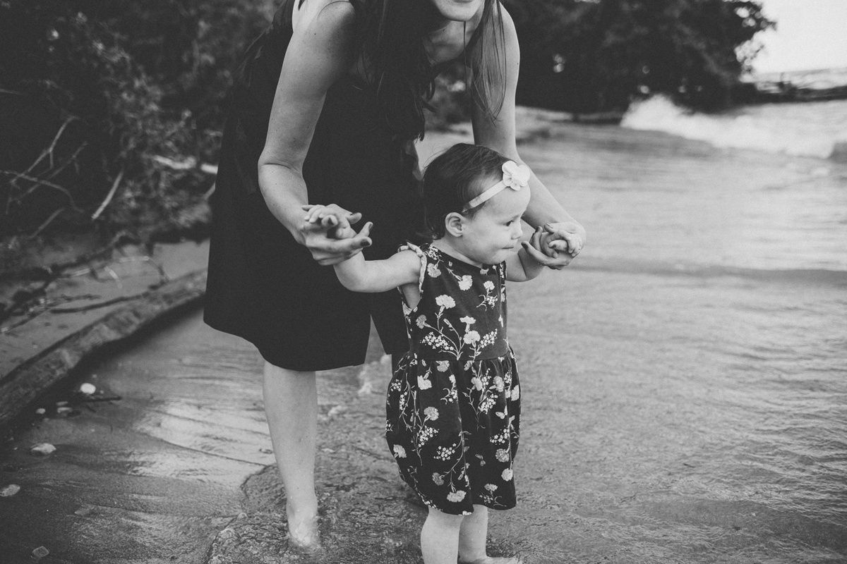 A black and white image of a parent and child exploring the beach together.