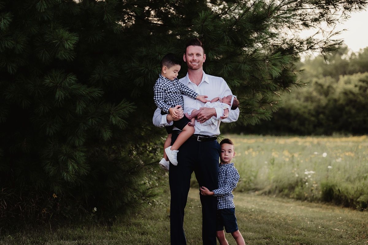 Family portrait against evergreen trees in soft evening light.