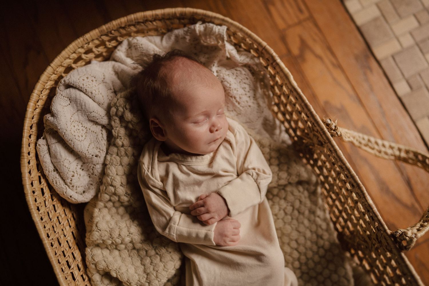 A sleeping newborn baby rests peacefully in a woven basket on a wooden floor.