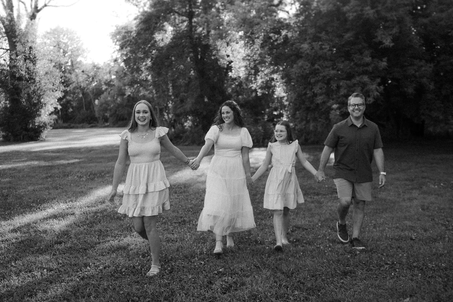 Black and white image of a family walking together on a tree-lined path.